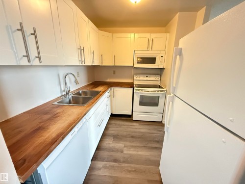 Kitchen featuring white cabinetry with brushed nickel hardware, wood-finish countertops, and a dual stainless steel sink - 706 10125 109 Street, Edmonton, AB 