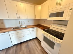 Kitchen featuring white shaker-style cabinetry, wood-finish countertops, stainless steel double-basin sink with a gooseneck faucet, white electric range, and wood-finish flooring - 