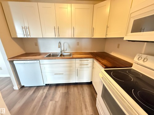 Kitchen featuring white shaker-style cabinetry, wood-finish countertops, stainless steel double basin sink with a high-arc faucet, and wood-finish flooring - 706 10125 109 Street, Edmonton, AB 