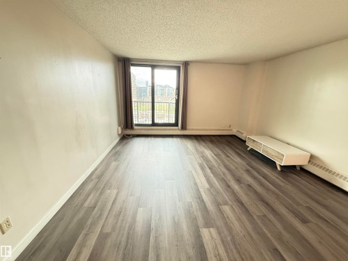 Spacious room featuring wood-finish flooring, a large window with vertical blinds, and a built-in wall heater - 706 10125 109 Street, Edmonton, AB 