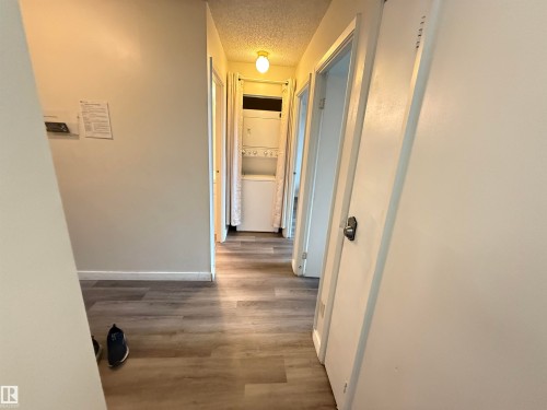 Hallway featuring wood-finish flooring, light-toned walls, and a recessed laundry area with a stacked washer and dryer unit - 706 10125 109 Street, Edmonton, AB 