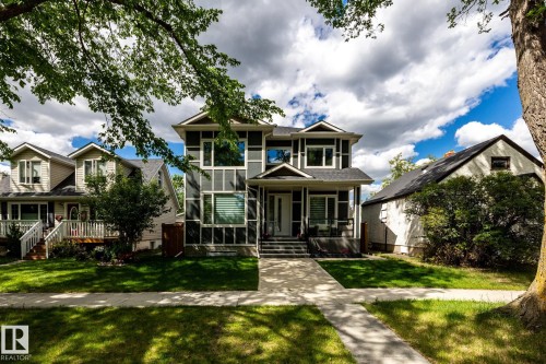 Contemporary residence featuring a prominent two-story window wall, dark exterior siding, a covered front porch, and a well-maintained front lawn - 10936 71 Avenue, Edmonton, AB 