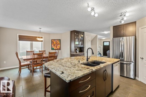 Open-concept kitchen featuring a granite countertop island with double sink, stainless steel appliances, dark wood cabinetry, and track lighting - 1086 Grantham Drive, Edmonton, AB 
