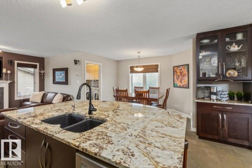 Kitchen island featuring a dual basin sink with a matte black high-arc faucet, granite countertops, and dark wood cabinetry - 1086 Grantham Drive, Edmonton, AB 