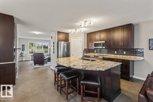Kitchen featuring a large, irregularly shaped island with a stone countertop, dark wood cabinetry, stainless steel appliances, and a subway tile backsplash - 1086 Grantham Drive, Edmonton, AB 