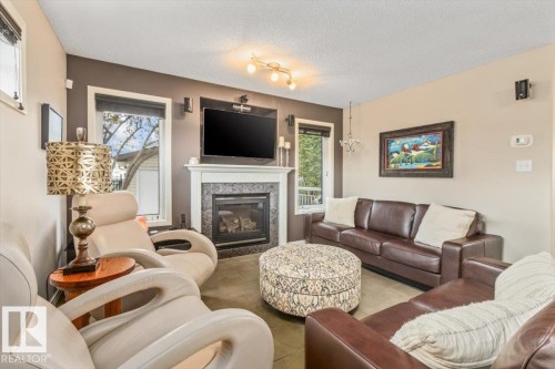 Living area featuring a fireplace with a white mantel and dark stone surround, large windows with blinds, and tile flooring - 1086 Grantham Drive, Edmonton, AB 