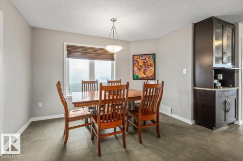 Dining area featuring tiled flooring, a pendant light fixture, and a built-in dark wood cabinetry unit with glass display doors and a stone countertop - 1086 Grantham Drive, Edmonton, AB 