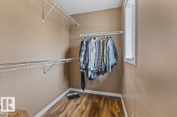 Walk-in closet featuring wood-finish flooring, neutral wall paint, white trim, and a window for natural light - 