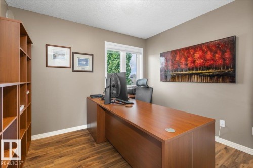 Dedicated office space featuring wood-finish flooring, a built-in shelving unit, a large window, and neutral wall tones - 1086 Grantham Drive, Edmonton, AB 