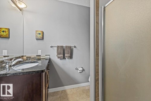 Bathroom vanity featuring a dark wood-finish cabinet with an undermount sink, granite countertop, and mosaic tile backsplash - 1086 Grantham Drive, Edmonton, AB 