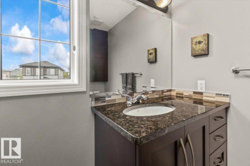 Vanity with a dark stone-finish countertop, undermount sink, and a multi-tone tile backsplash - 1086 Grantham Drive, Edmonton, AB 