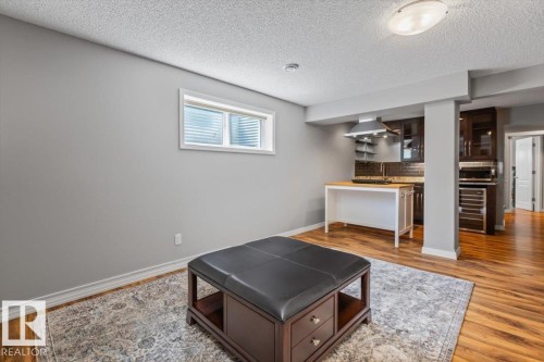 Lower level living area featuring wood-finish flooring, a contemporary wet bar with dark cabinetry, stainless steel range hood, built-in wine cooler, and recessed lighting - 1086 Grantham Drive, Edmonton, AB 