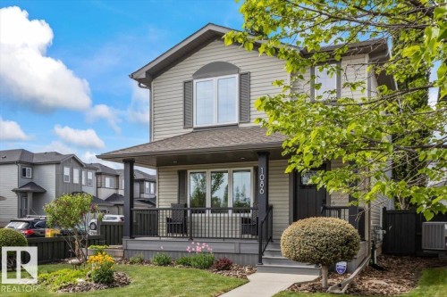 Two-story residence featuring light-colored siding, a covered front porch with dark railings, and prominent upper-level windows with dark shutters - 1086 Grantham Drive, Edmonton, AB 