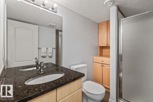 Bathroom featuring a dual sink vanity with a dark speckled countertop, light wood-finish cabinetry, and a walk-in shower with frosted glass enclosure - 1086 Grantham Drive, Edmonton, AB 