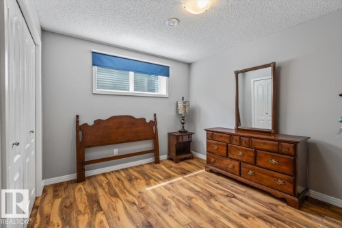 Bedroom featuring wood-finish flooring, a window with a blue roller shade, light gray walls, and a white bi-fold closet door - 1086 Grantham Drive, Edmonton, AB 