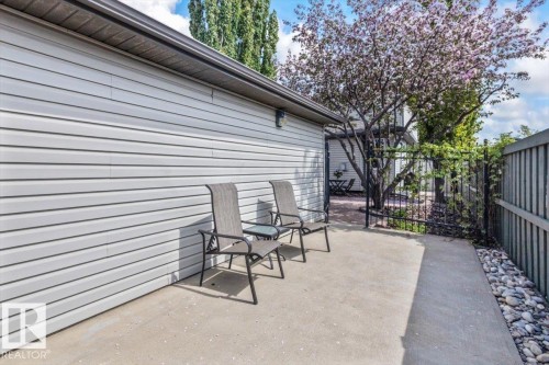 Concrete patio area with light gray siding, a black metal fence, and a mature flowering tree - 1086 Grantham Drive, Edmonton, AB 