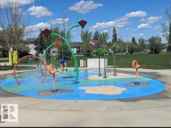 Community splash pad featuring multiple water features, a colorful ground surface, and surrounding green space - 