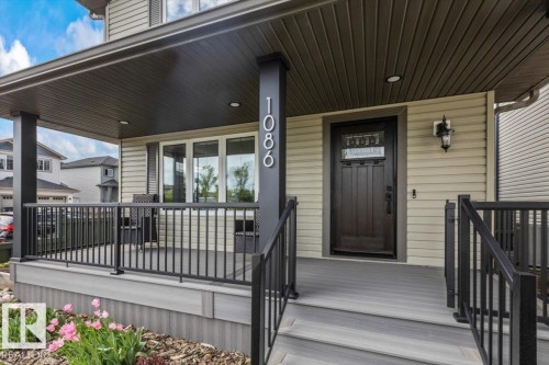 Covered front porch featuring composite decking, black aluminum railings, recessed ceiling lighting, and a dark wood-finish entry door with decorative glass - 1086 Grantham Drive, Edmonton, AB 