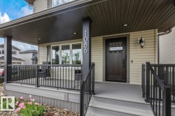 Covered front porch featuring composite decking, black aluminum railings, recessed ceiling lighting, and a dark wood-finish entry door with decorative glass - 