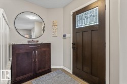 Entryway featuring a dark wood-finish door with leaded glass, tile flooring, and a built-in cabinetry unit with a granite countertop and satin nickel hardware - 