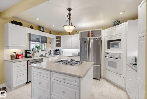 Kitchen featuring white cabinetry, light-toned countertops, a central island with a built-in cooktop, stainless steel refrigerator, and integrated wall oven with microwave - 78 Goodridge Drive, St. Albert, AB 