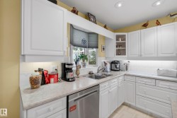 Kitchen featuring white cabinetry, light countertops, a stainless steel dishwasher, and a bay window - 