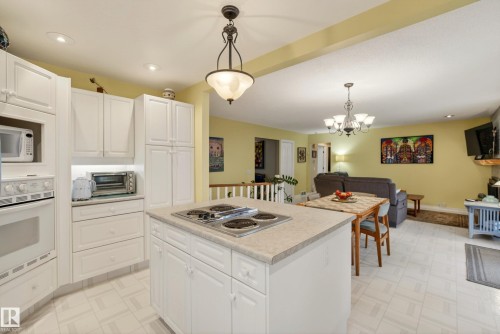Kitchen featuring white cabinetry, an island with an integrated cooktop, light-toned countertops, and a built-in oven - 78 Goodridge Drive, St. Albert, AB 