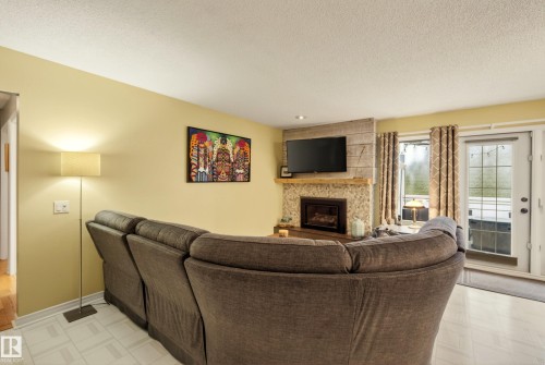 Living area featuring a stone fireplace with a wood mantle, recessed lighting, and a wall-mounted television - 78 Goodridge Drive, St. Albert, AB 