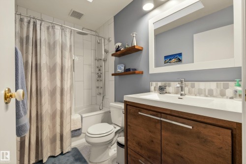Bathroom featuring a wood-finish vanity with an integrated sink, a tiled backsplash, and an overhead mirror with integrated lighting - 78 Goodridge Drive, St. Albert, AB 