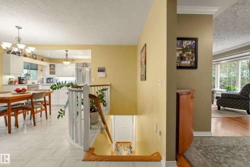 Open concept main level featuring a white kitchen with upper and lower cabinetry, a dining area with a chandelier, a staircase with white spindles, and wood-finish flooring in the foreground - 78 Goodridge Drive, St. Albert, AB 