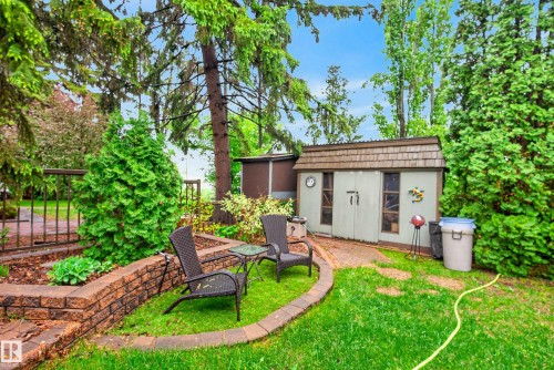 Manicured lawn area with a stone block retaining wall, mature trees, and a garden shed with a shingled roof - 78 Goodridge Drive, St. Albert, AB 