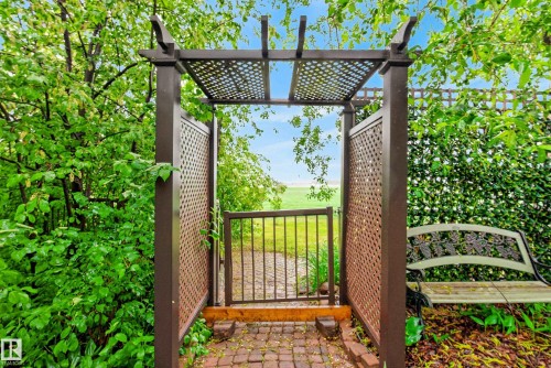 Arbor entry with a lattice screen and gate leading to an open field - 78 Goodridge Drive, St. Albert, AB 