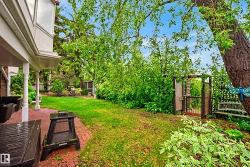 Expansive backyard featuring a brick paver patio, lush green lawn, mature trees, and a decorative garden gate - 78 Goodridge Drive, St. Albert, AB 