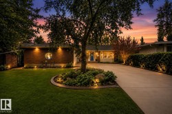 Brick and siding exterior featuring a round window, mature landscaping, a concrete driveway, and integrated exterior lighting - 