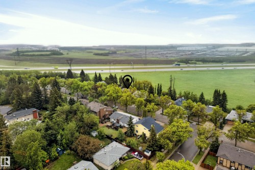 Aerial perspective showcasing a residential area with mature trees and varied roofing materials, bordering expansive green fields - 78 Goodridge Drive, St. Albert, AB 