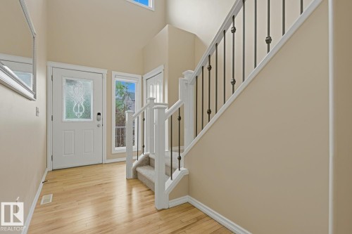 Foyer featuring wood-finish flooring, a white front door with decorative glass, and a staircase with white balusters and black metal spindles - 11612 11 Avenue, Edmonton, AB - Indoor Photo Showing Other Room