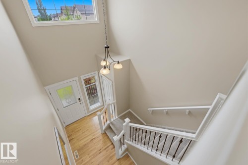 Two-story foyer featuring wood-finish flooring, a contemporary chandelier, a transom window, and a staircase with carpeted treads and wrought iron balusters - 11612 11 Avenue, Edmonton, AB - Indoor Photo Showing Other Room