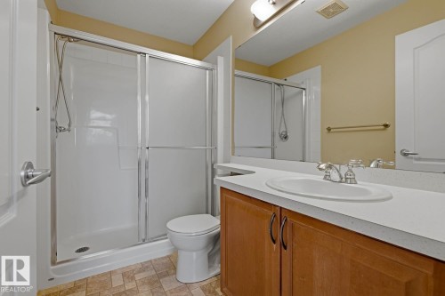 Bathroom featuring a shower with sliding glass doors, a vanity with a white countertop and integrated sink, a wood-finish cabinet, and a large wall-mounted mirror - 11612 11 Avenue, Edmonton, AB - Indoor Photo Showing Bathroom