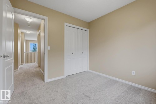 Neutral-toned room featuring a soft gray carpet, white bi-fold closet doors, and a doorway leading to a carpeted hallway with a railing - 11612 11 Avenue, Edmonton, AB - Indoor Photo Showing Other Room