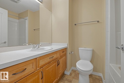 Bathroom featuring a wood-finish vanity with a white countertop and integrated sink, a large wall-mounted mirror, a white toilet, and patterned floor tiling - 11612 11 Avenue, Edmonton, AB - Indoor Photo Showing Bathroom