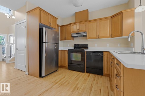 Kitchen featuring wood-finish flooring, light wood cabinetry, stainless steel refrigerator, black range, and white countertops - 11612 11 Avenue, Edmonton, AB - Indoor Photo Showing Kitchen With Double Sink