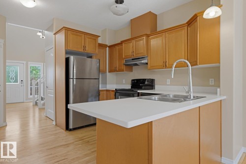 Kitchen featuring light wood-finish cabinetry, stainless steel appliances, a double basin sink, light countertops, and wood-finish flooring - 11612 11 Avenue, Edmonton, AB - Indoor Photo Showing Kitchen With Double Sink