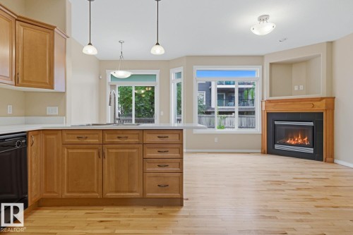 Kitchen island with light wood cabinetry, white countertops, and three pendant light fixtures - 11612 11 Avenue, Edmonton, AB - Indoor With Fireplace