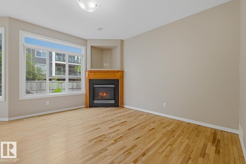 Spacious room featuring wood-finish flooring, a corner fireplace with a wood mantle and built-in alcove, and large windows - 11612 11 Avenue, Edmonton, AB - Indoor Photo Showing Living Room With Fireplace