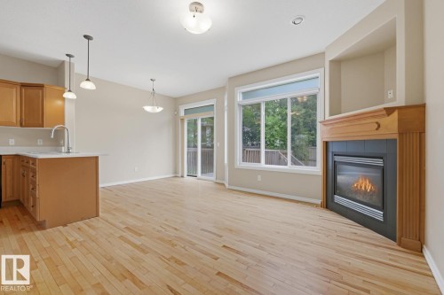 Open-concept living area with wood-finish flooring, a built-in fireplace featuring a black tile surround and wood mantel, and large windows providing natural light - 11612 11 Avenue, Edmonton, AB - Indoor With Fireplace