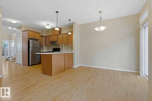 Open-concept kitchen and dining area featuring light wood-finish flooring, a kitchen island with a white countertop, and stainless steel appliances - 11612 11 Avenue, Edmonton, AB - Indoor Photo Showing Kitchen