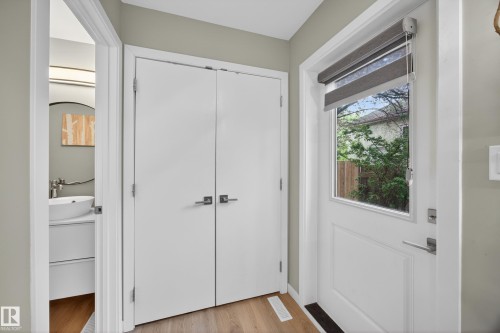 Entryway featuring a paneled door with an integrated window, light wood-finish flooring, and a double-door closet with contemporary hardware - 12604 116 Avenue, Edmonton, AB 