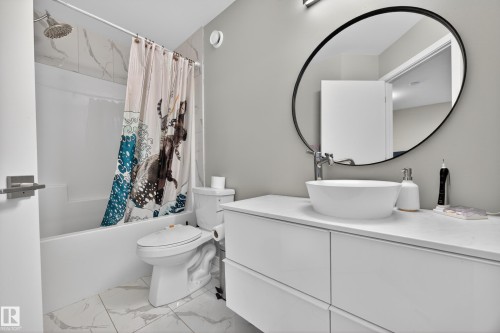 Bathroom featuring a white vanity with vessel sink, oval mirror, and a shower-tub combination with tile surround - 12604 116 Avenue, Edmonton, AB 