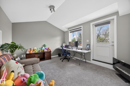 Spacious room featuring sloped ceilings, two windows with roller blinds, a door with exterior access, and neutral gray walls - 12604 116 Avenue, Edmonton, AB 