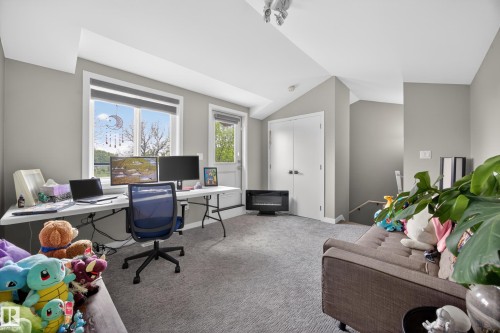 Carpeted multi-purpose room with a sloped ceiling, featuring a large window, an exterior door, and a built-in closet with double doors - 12604 116 Avenue, Edmonton, AB 